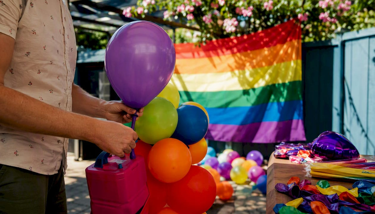 Hands inflating balloons beside Pride flag backdrop